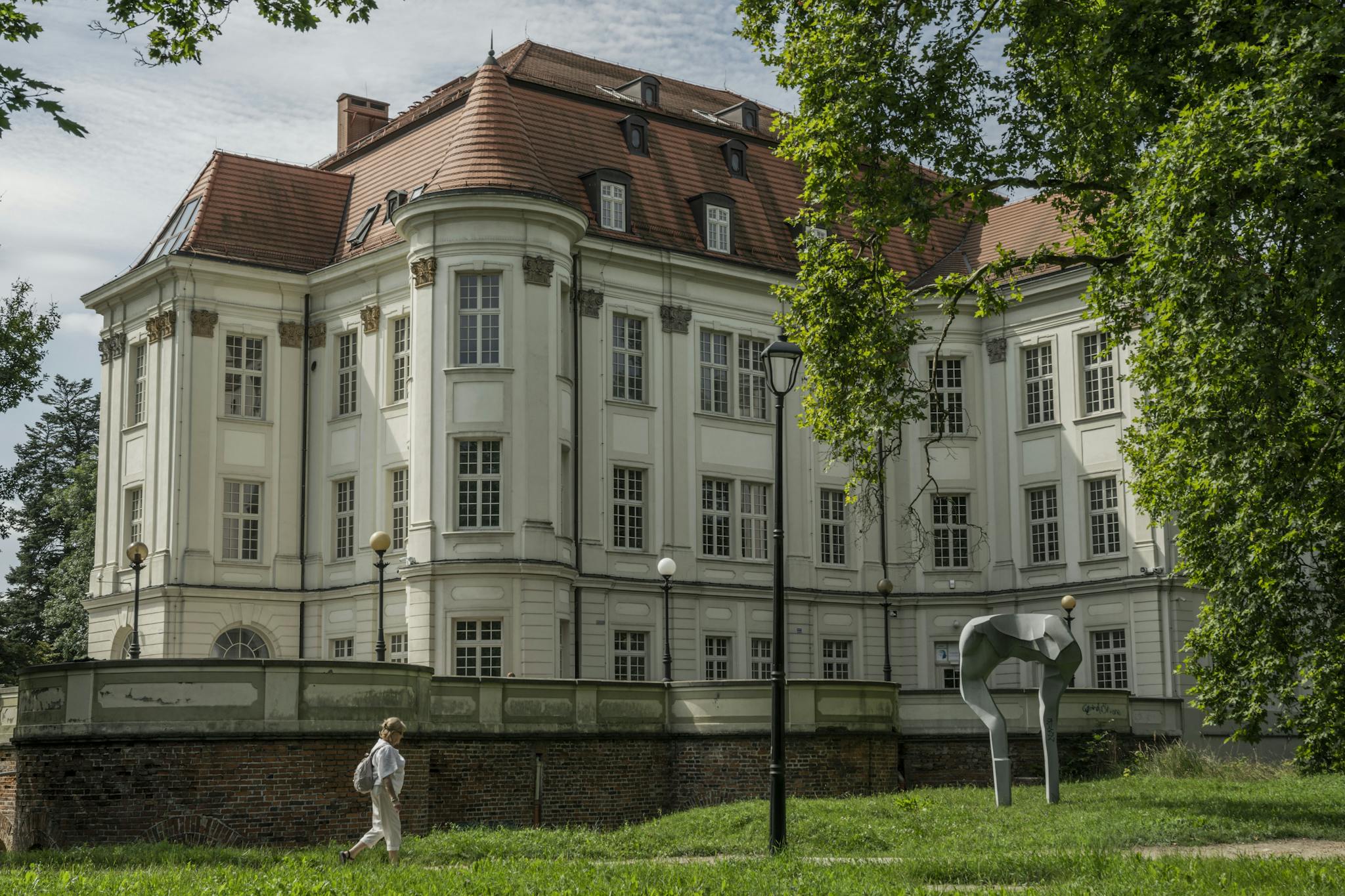 Elegant historic mansion with contemporary sculpture in a lush Wrocław park, capturing timeless beauty and modern art.